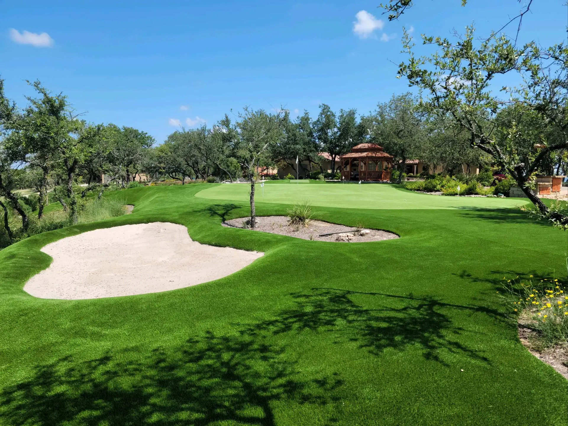 Aerial view of a custom golf complex with multiple greens, bunkers, chipping areas, and a running creek by Celebrity Greens®
