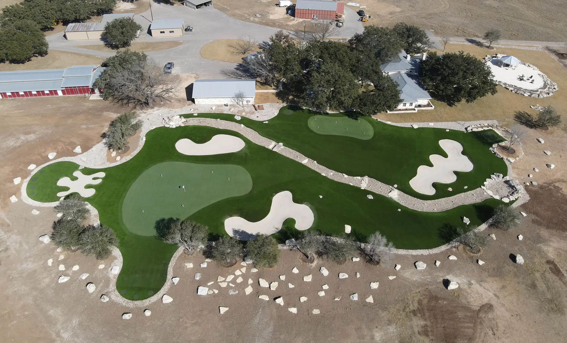 Aerial view of a custom golf complex with multiple greens, bunkers, chipping areas, and a running creek by Celebrity Greens®