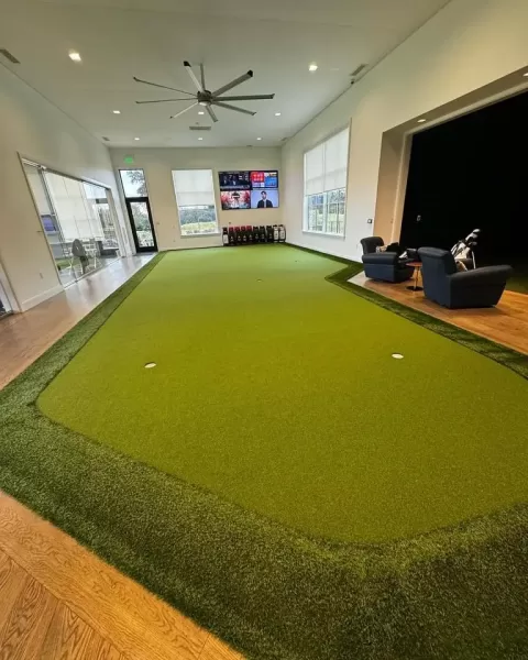 A long indoor putting green inside a house with windows overlooking the backyard