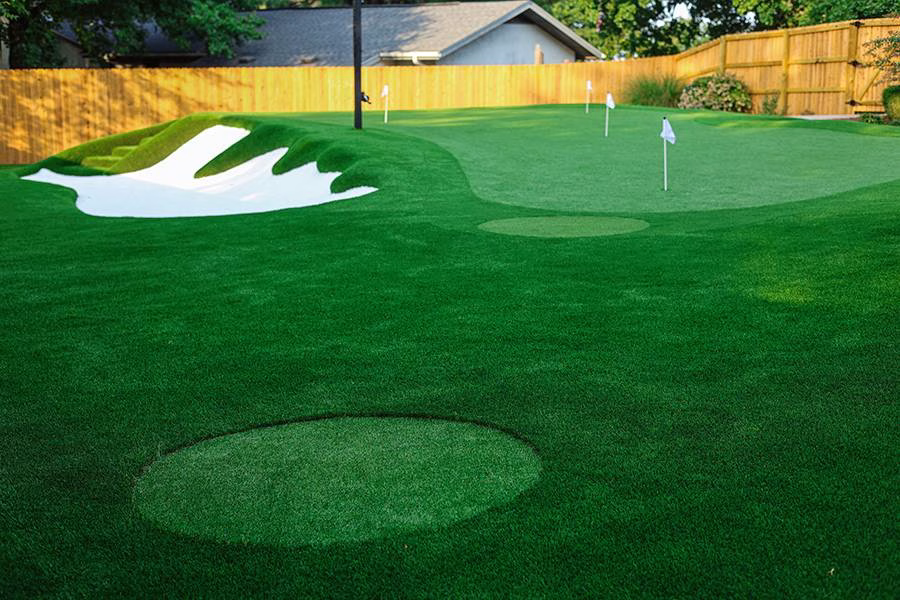 Artificial backyard putting green with multiple holes, sand bunker, and undulating terrain.